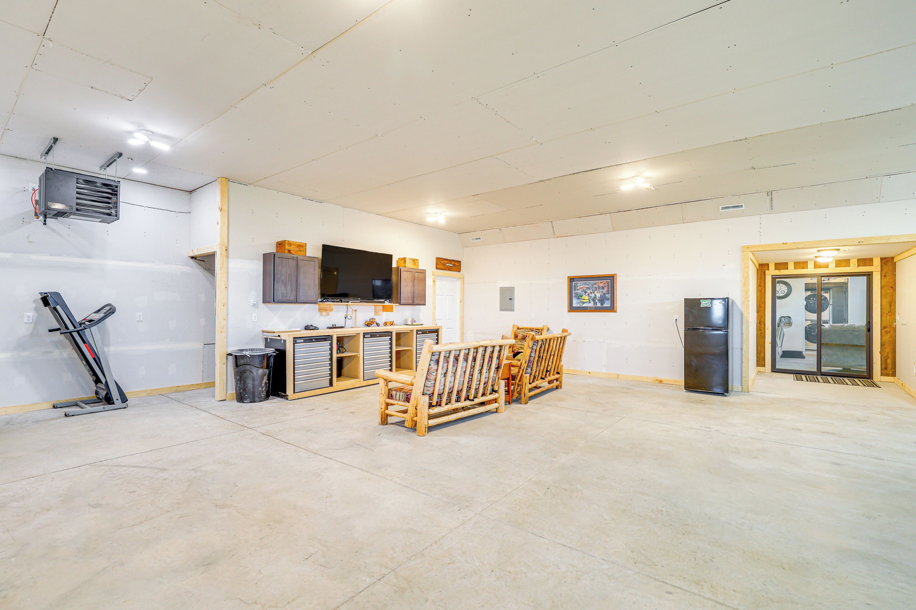 A spacious room with a large window, a wooden bench, a television, and a refrigerator.