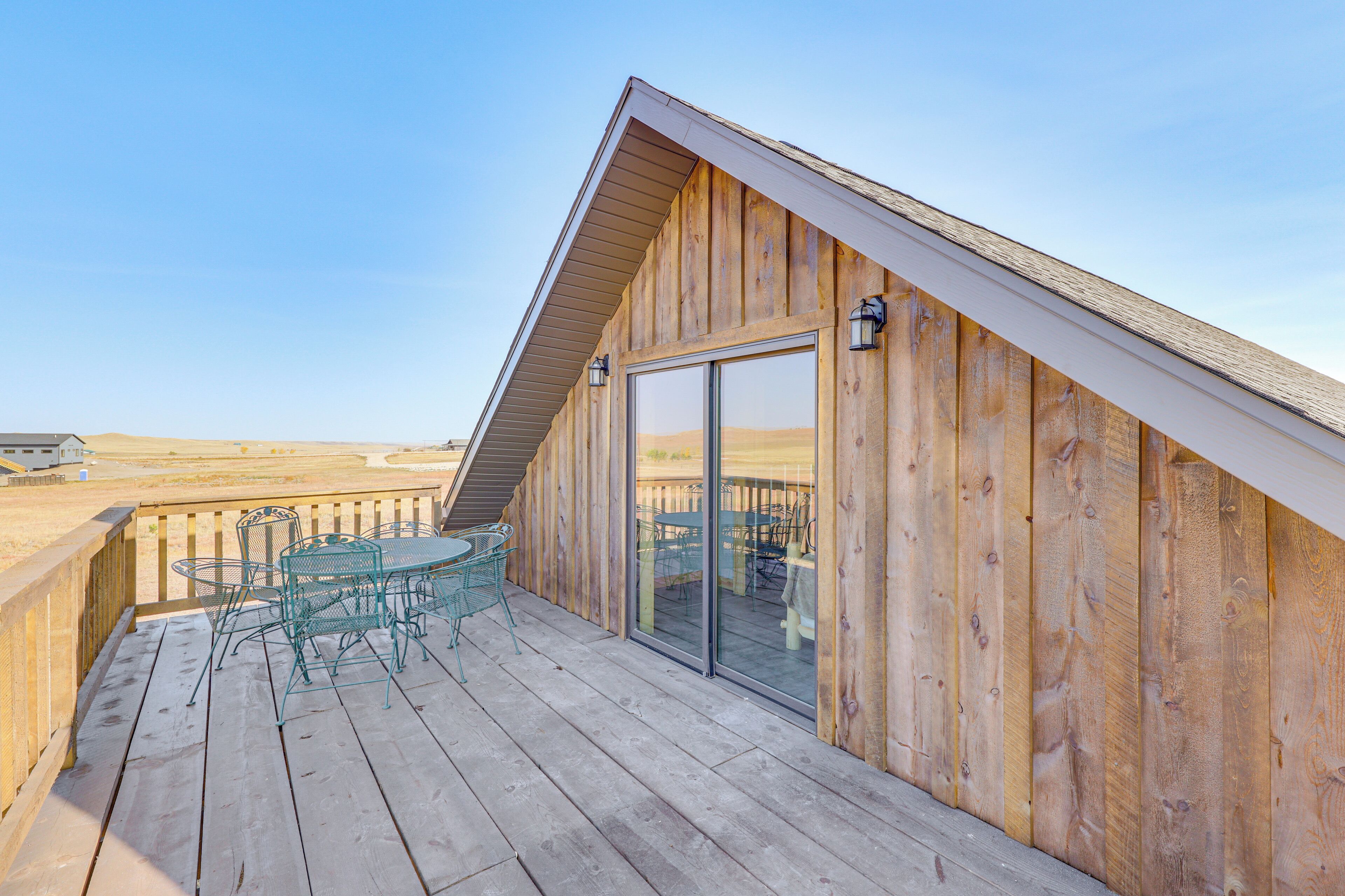 A wooden deck with a table and chairs, a glass door leading to an interior space, and a clear view of the surrounding landscape.