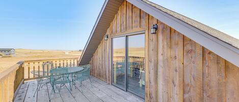 A wooden deck with a table and chairs, a glass door leading to an interior space, and a clear view of the surrounding landscape.
