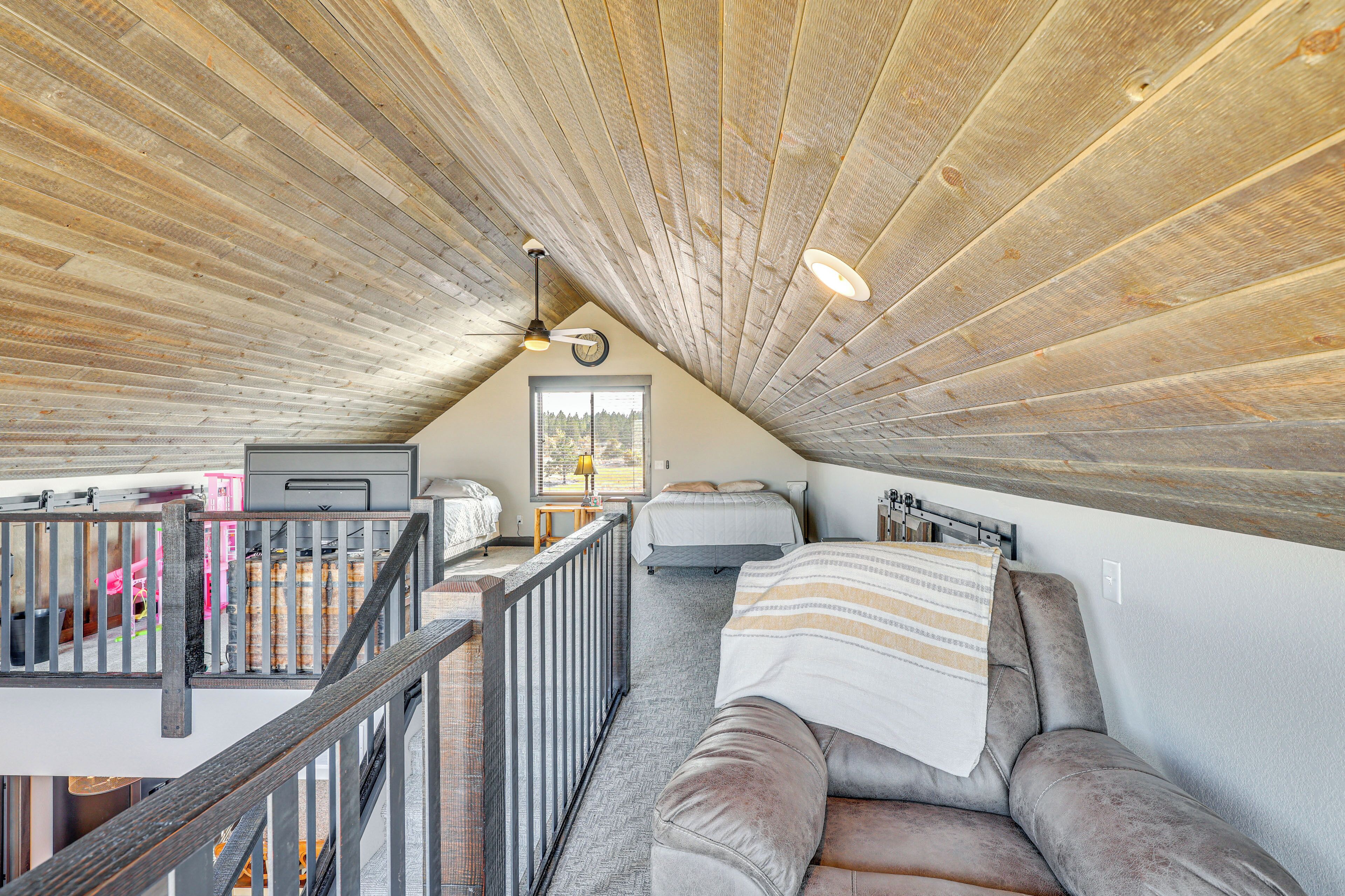 A loft bedroom with a sloped ceiling, a bed, a sofa, a desk, and a window with a view.