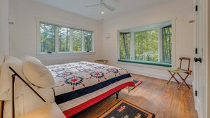 A bedroom with a bed, two windows, a ceiling fan, and a wooden floor. - Riverfront Hideaway in Keene: Walk to Town! (Keene)