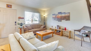A living room with a beige sofa, a wooden coffee table, a wicker chair, and a bookshelf with books and decorative items. - Mtn Views & Private Courtyard: Home in Pueblo West (Pueblo)