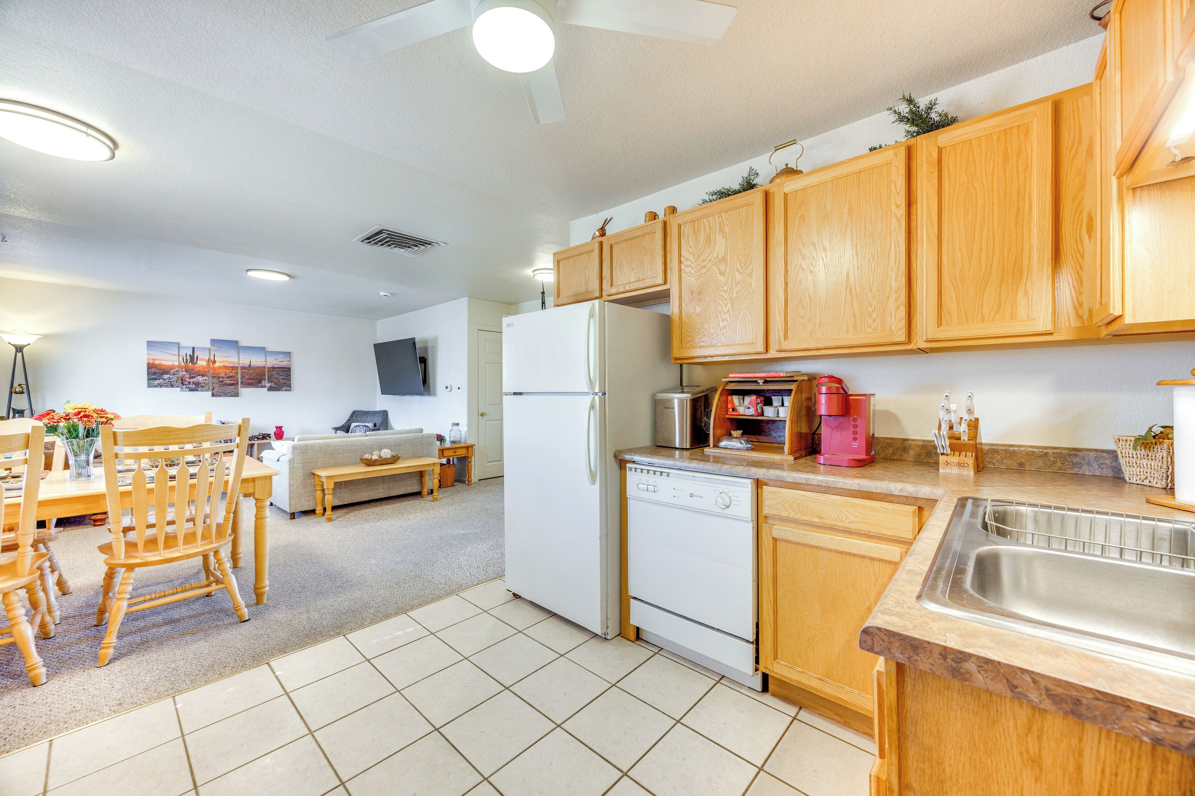 A modern kitchen with wooden cabinets, a white refrigerator, a dishwasher, and a coffee maker.