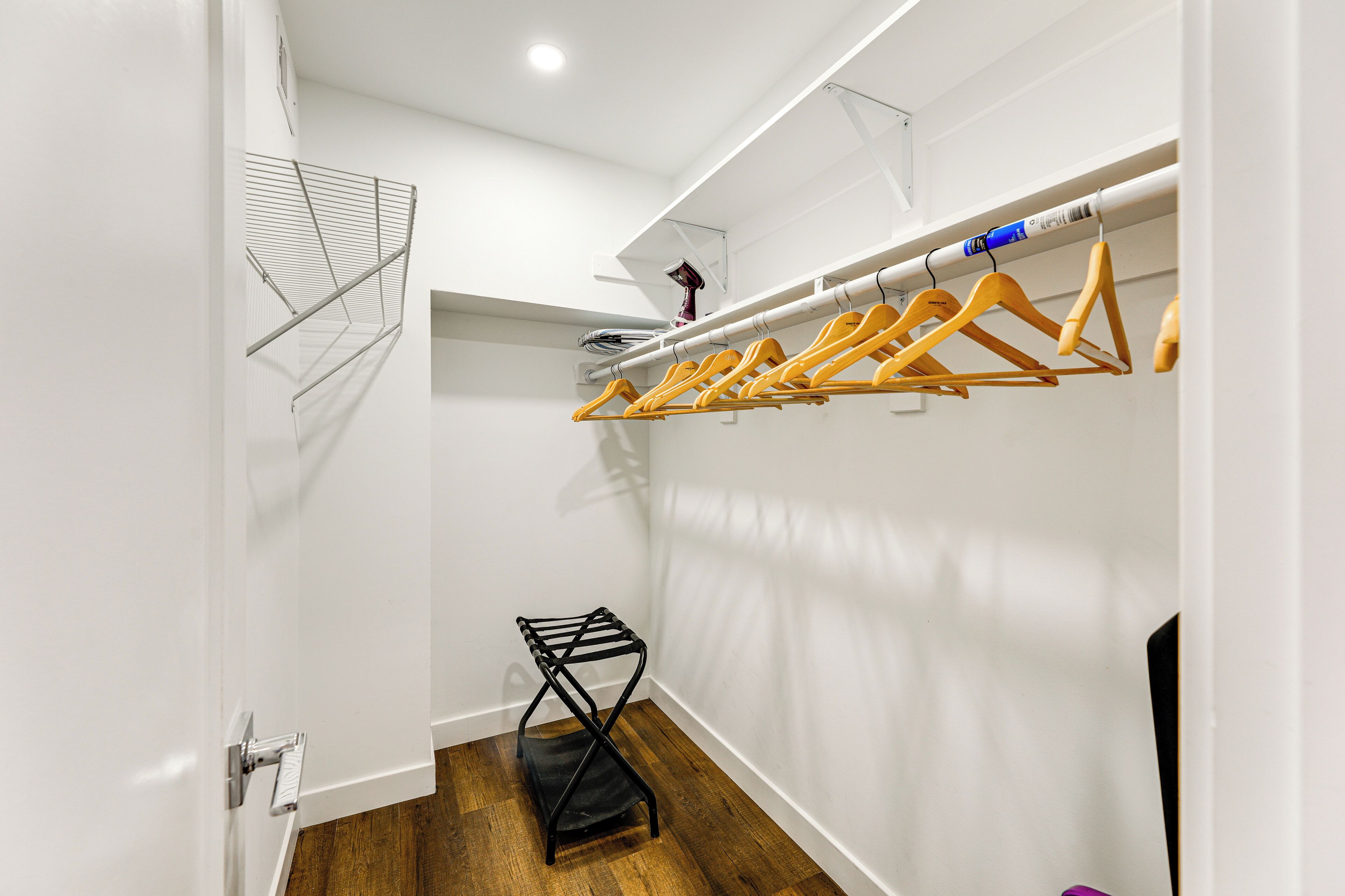 Un vestidor con perchas de madera y metal, un estante de metal negro y suelo de madera.