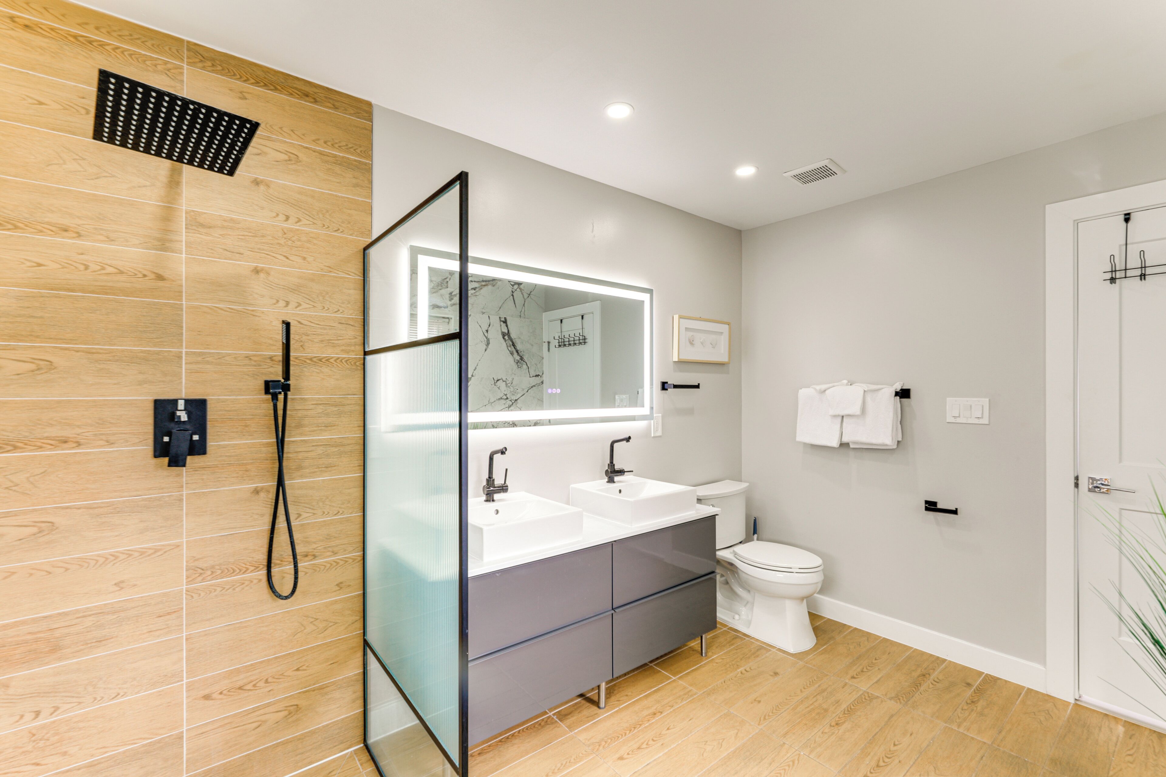 Un baño moderno con cabina de ducha de vidrio, inodoro blanco y tocador con un espejo grande.