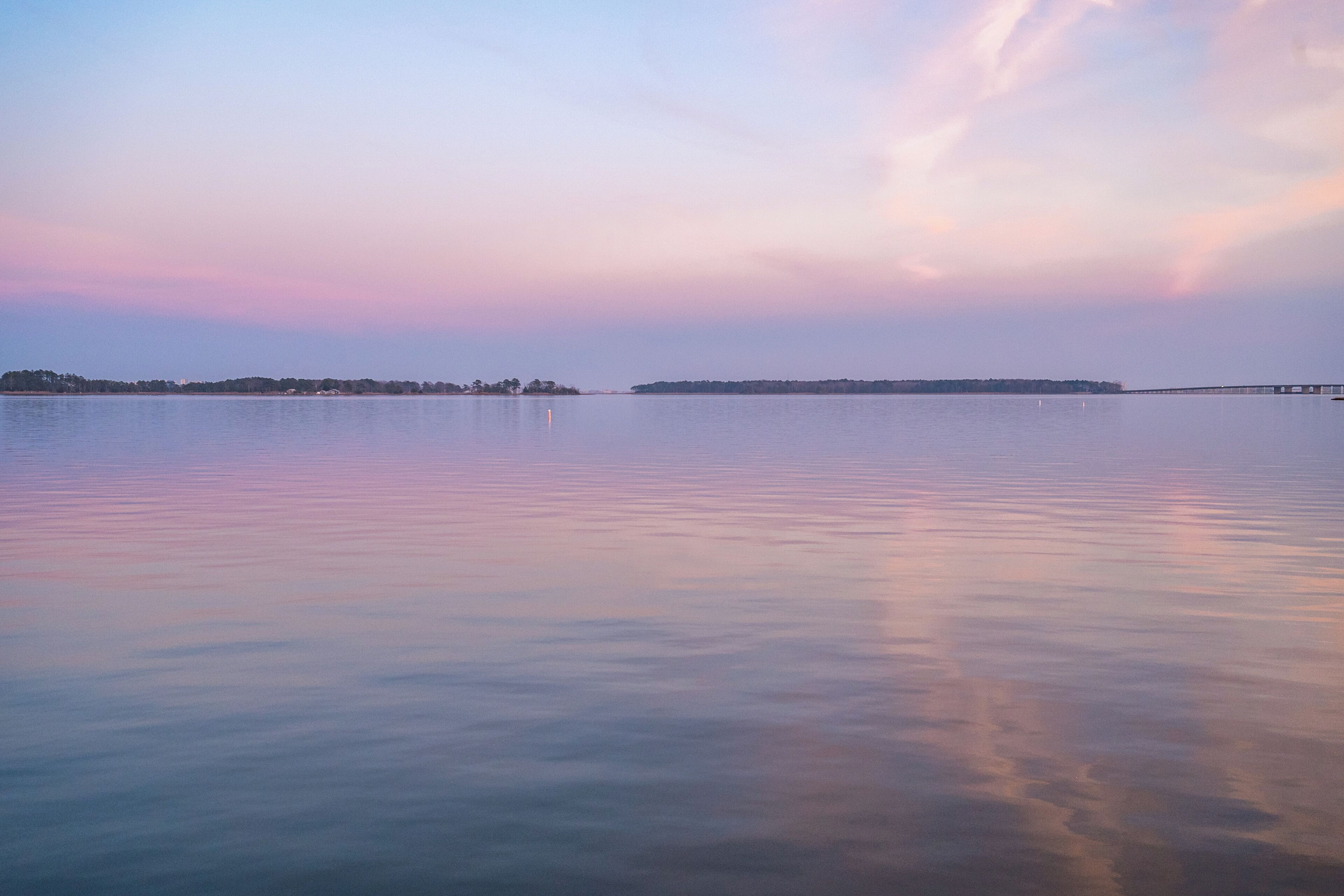 A calm lake with a distant shoreline and a bridge.