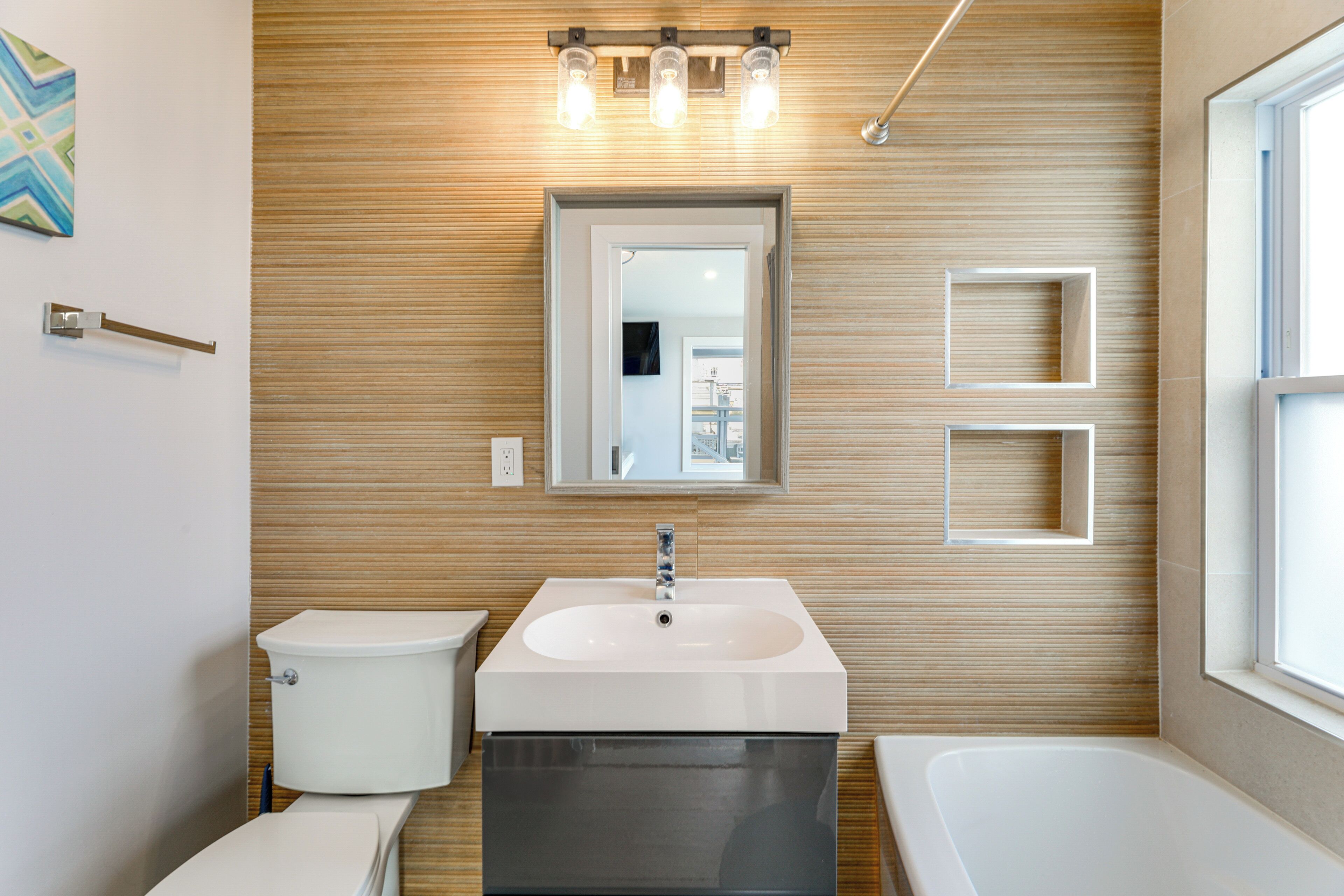 Un baño moderno con pared de madera, lavamanos blanco, inodoro y bañera.