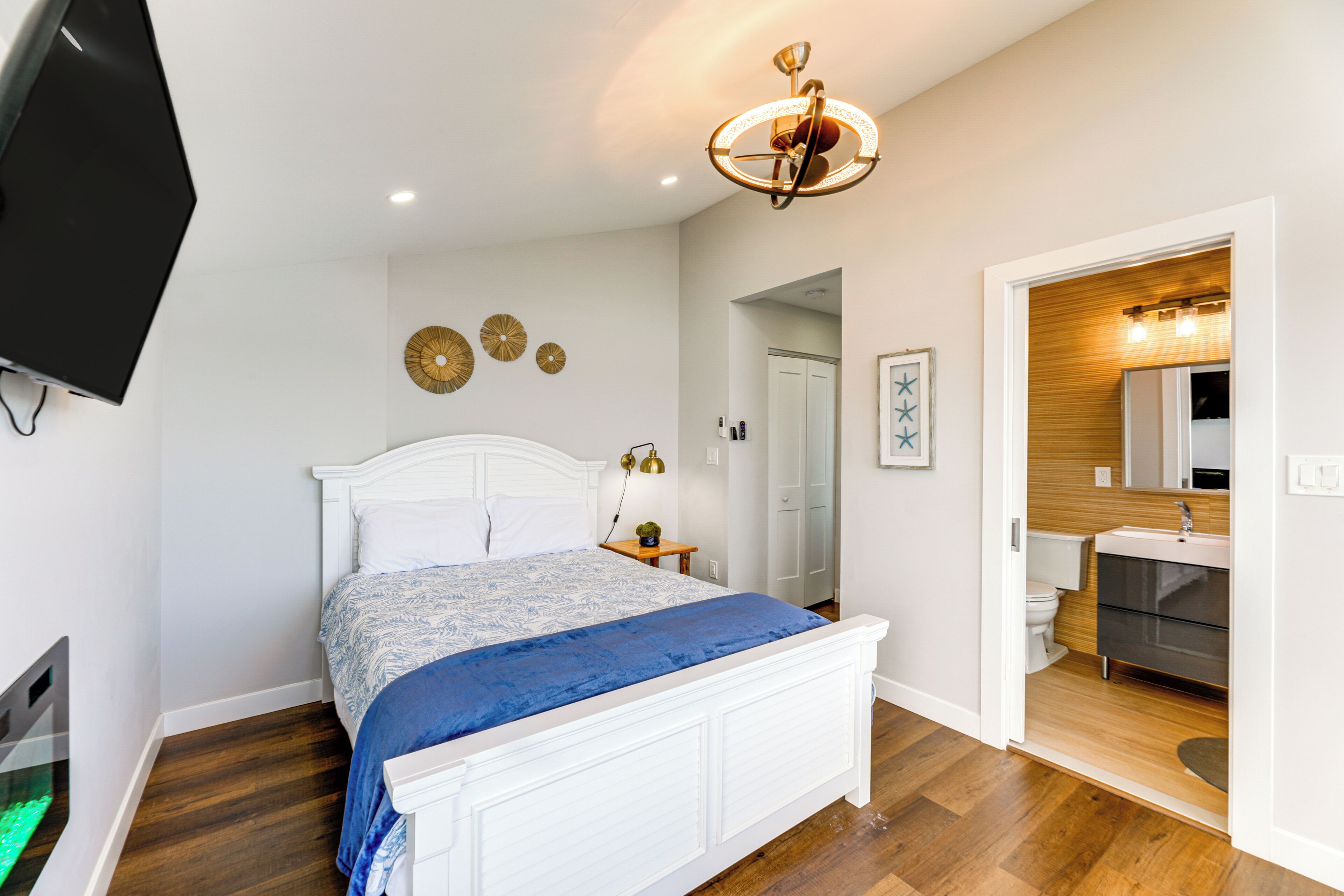 A bedroom with a bed, a television, a ceiling light fixture, and a bathroom visible through an open door.