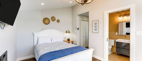 A bedroom with a bed, a television, a ceiling light fixture, and a bathroom visible through an open door.
