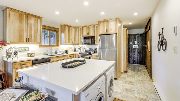 A modern kitchen with wooden cabinets, a stainless steel refrigerator, and a built-in washing machine.