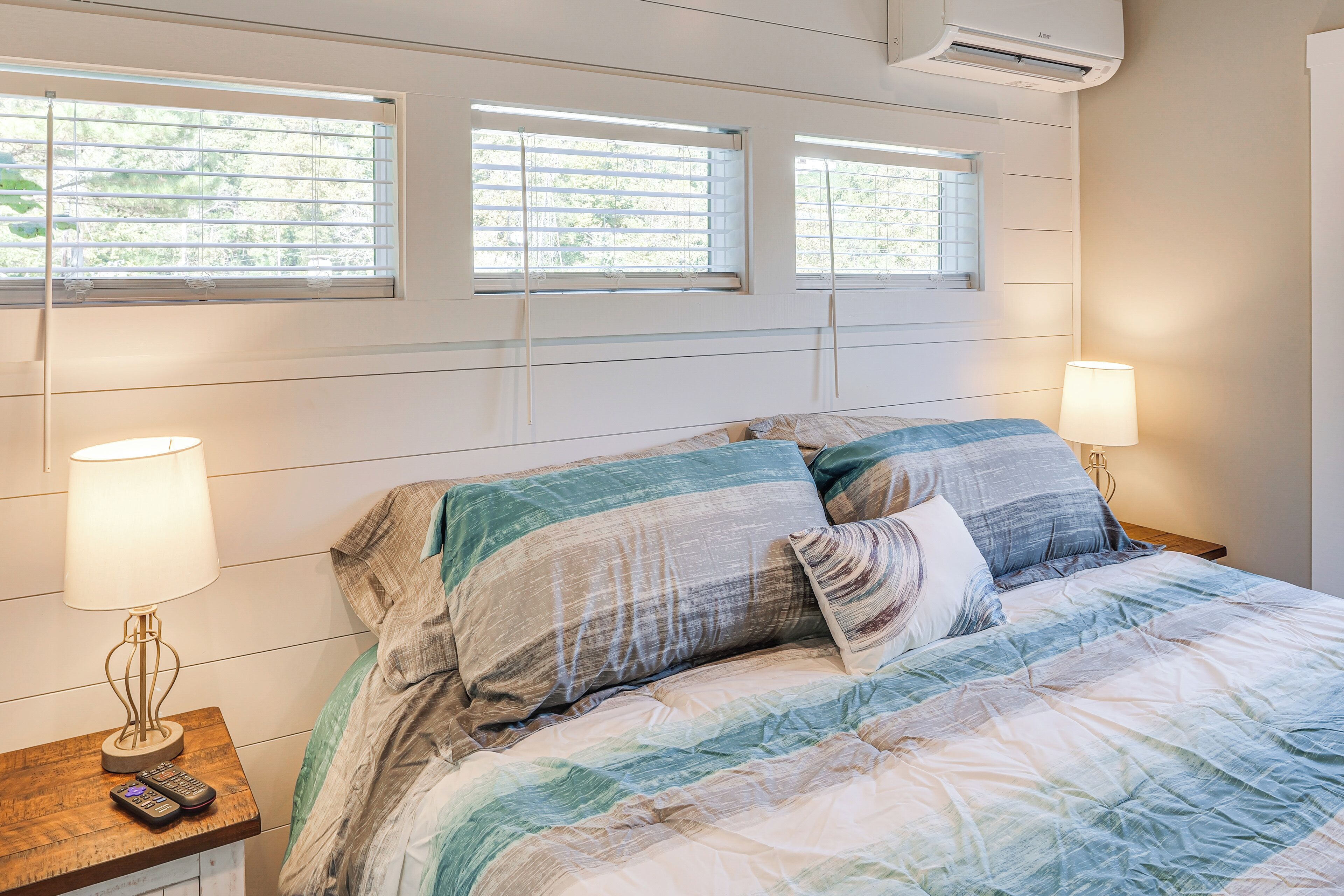 Een slaapkamer met een bed, twee bedlampen, een nachtkastje en een raam met jaloezieën.