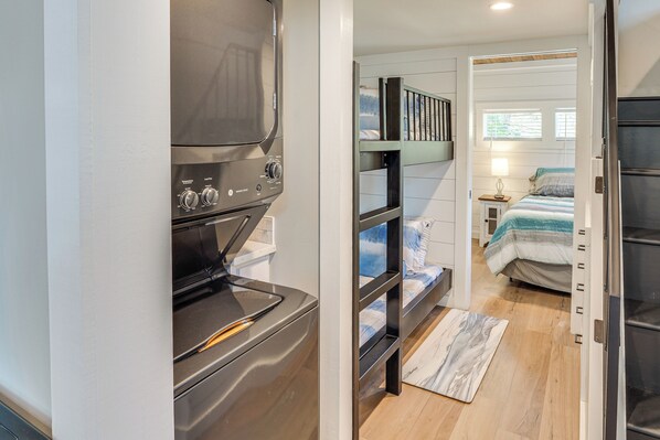 A compact kitchen with a built-in oven and a small countertop. A bunk bed with a blue and white striped blanket is visible in the adjacent bedroom.