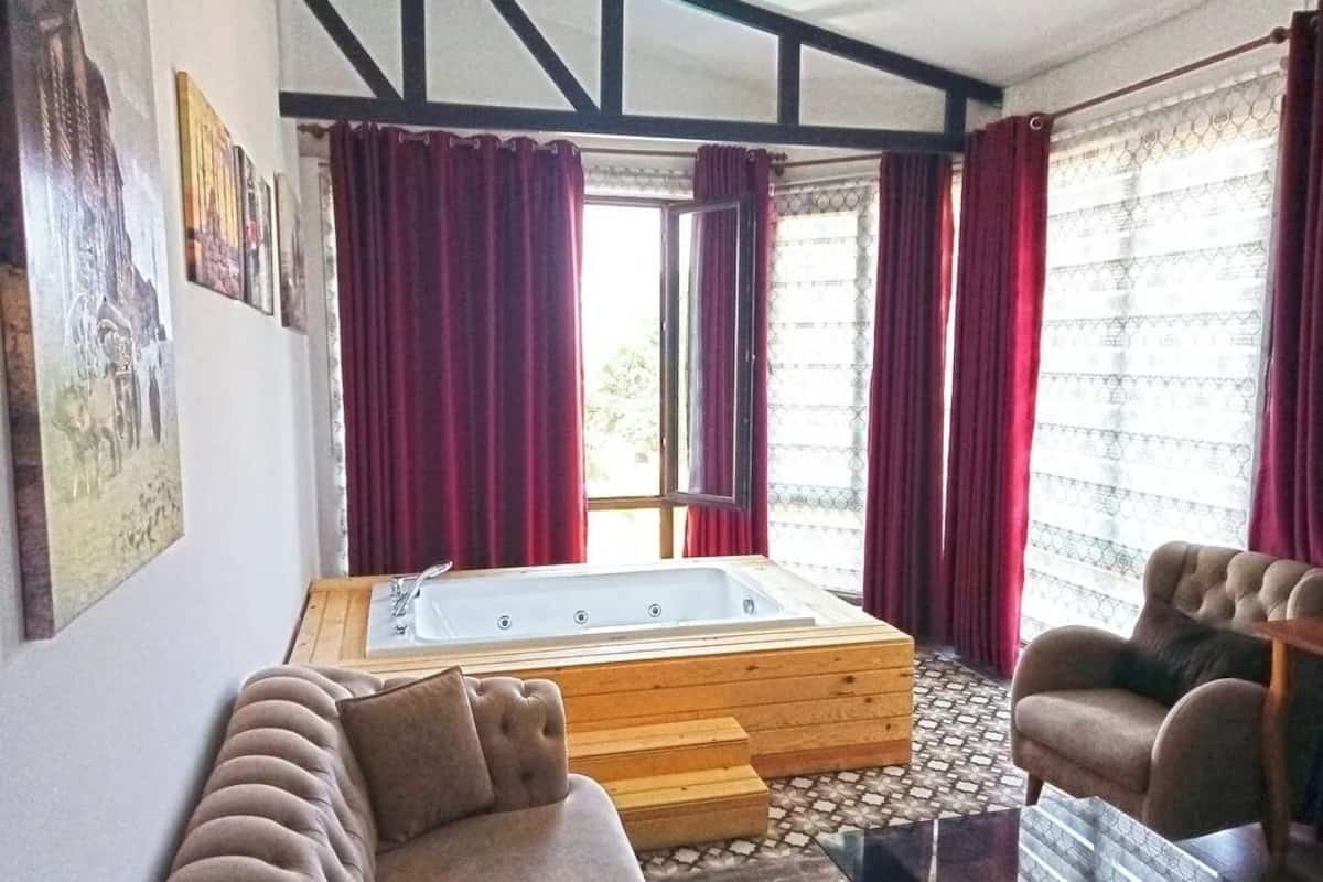 Una habitación con una bañera de madera, un sofá color beige y una silla.