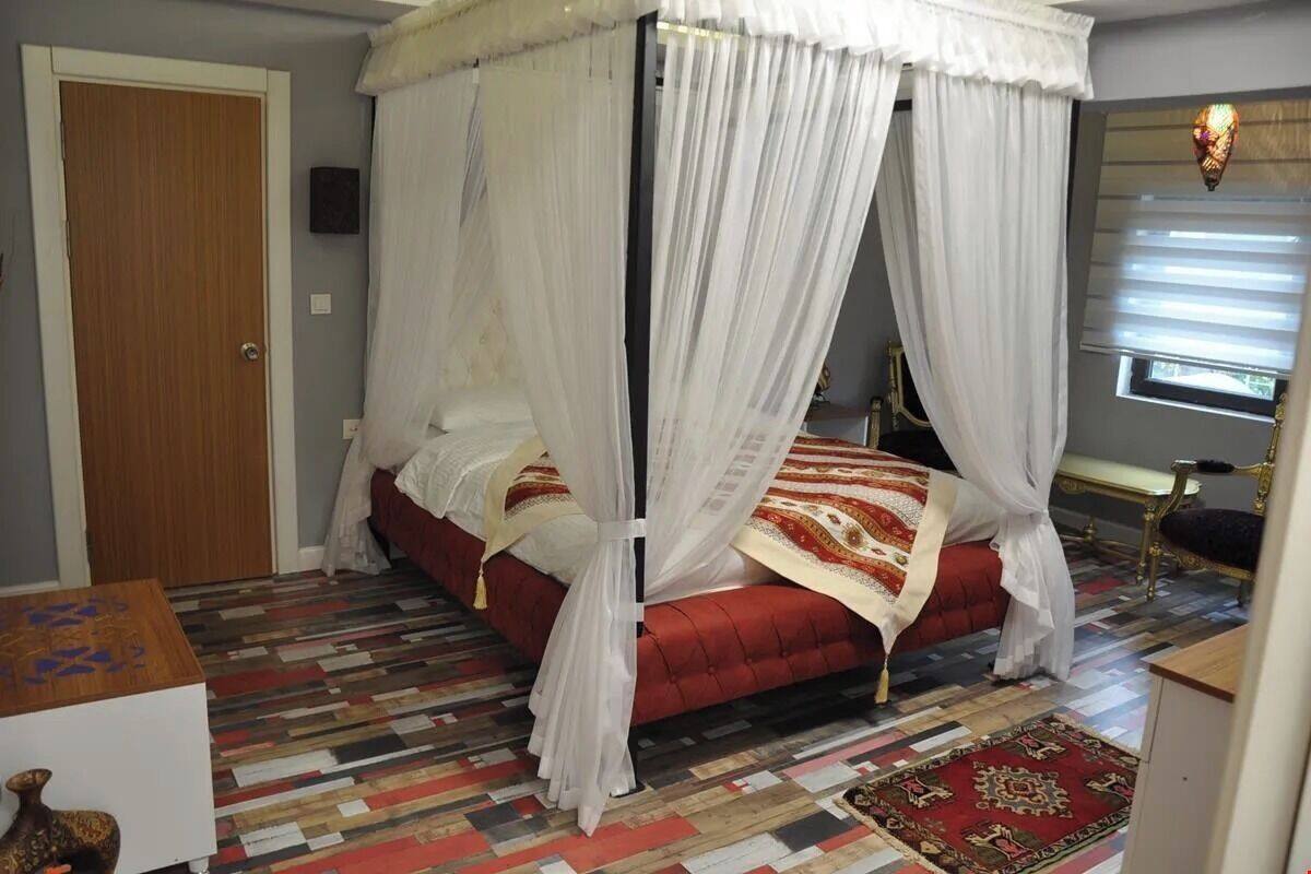 Un dormitorio con una cama con dosel, un tapete estampado y una pequeña mesa con un florero.