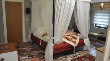 Un dormitorio con una cama con dosel, un tapete estampado y una pequeña mesa con un florero.