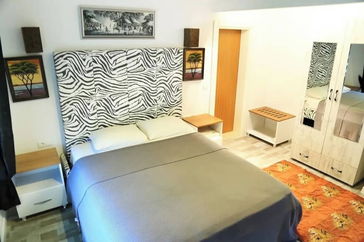 Un dormitorio con cabecera de estilo cebra, cama con cubierta gris, mesita de noche, armario con espejo y una pequeña mesa con bandeja.