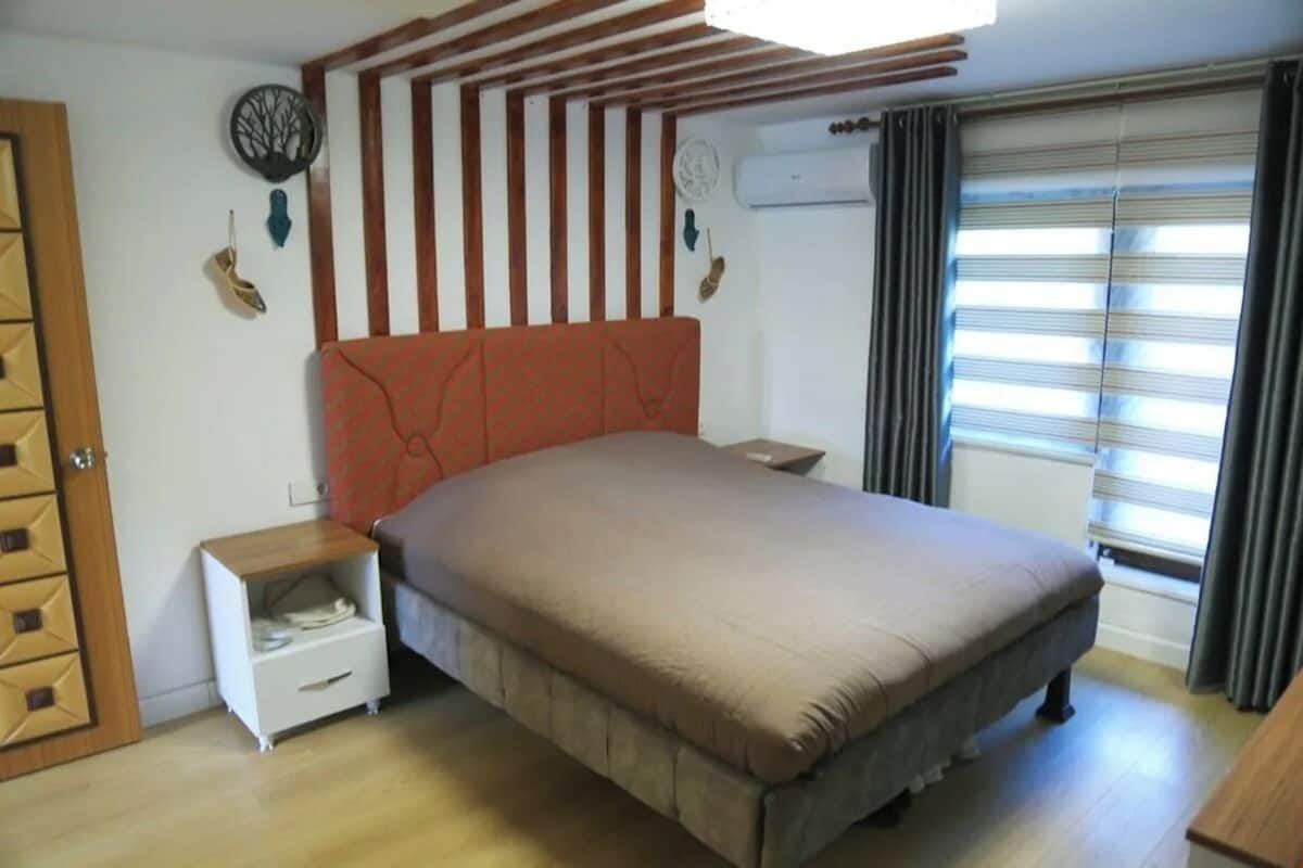 Un dormitorio con cama, mesita de noche, armario y ventana con cortinas.