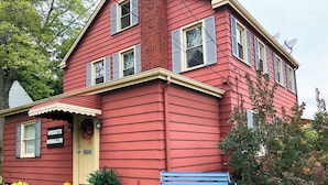 Une maison rouge à deux étages, avec une pancarte indiquant « BUCKEYE BUNGALOW », un banc et des plantes en pot.