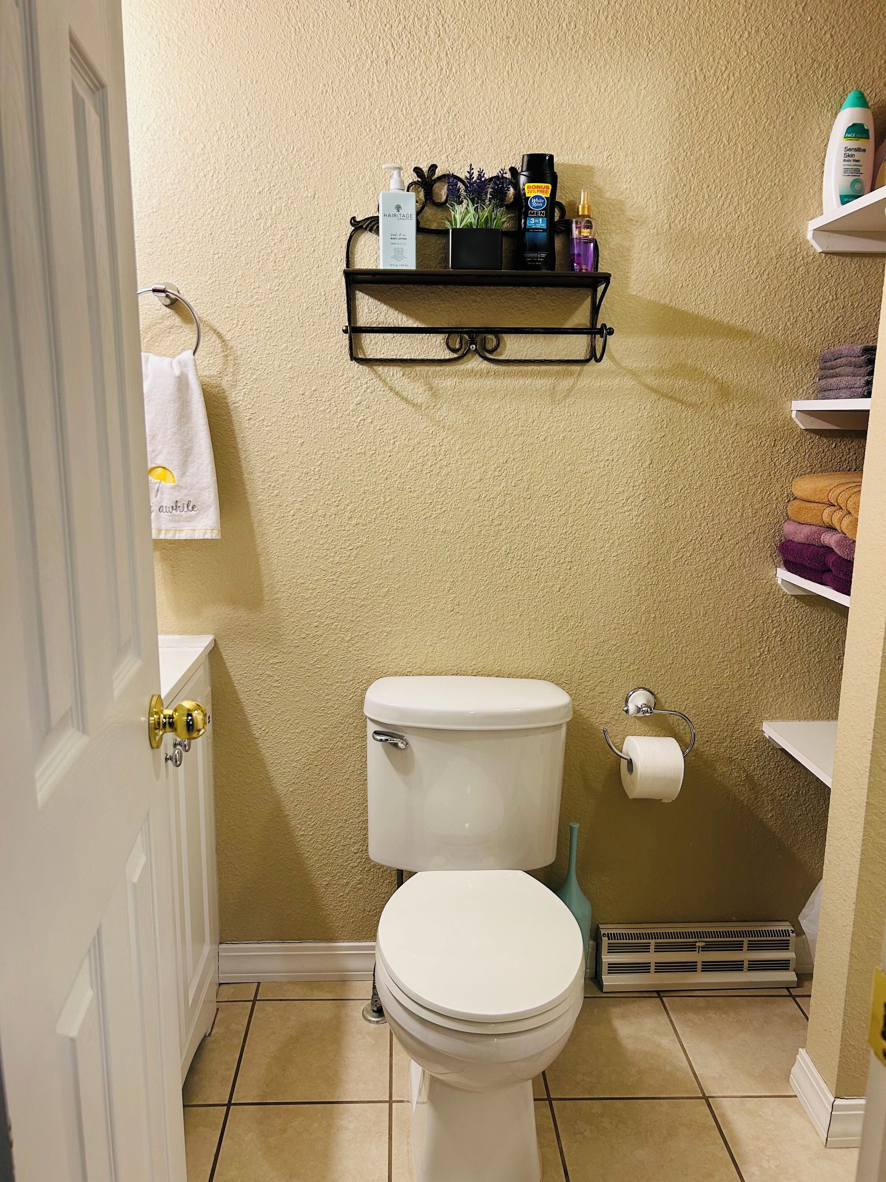 A bathroom with a toilet, a shelf with toiletries, and a towel hanging on the door.