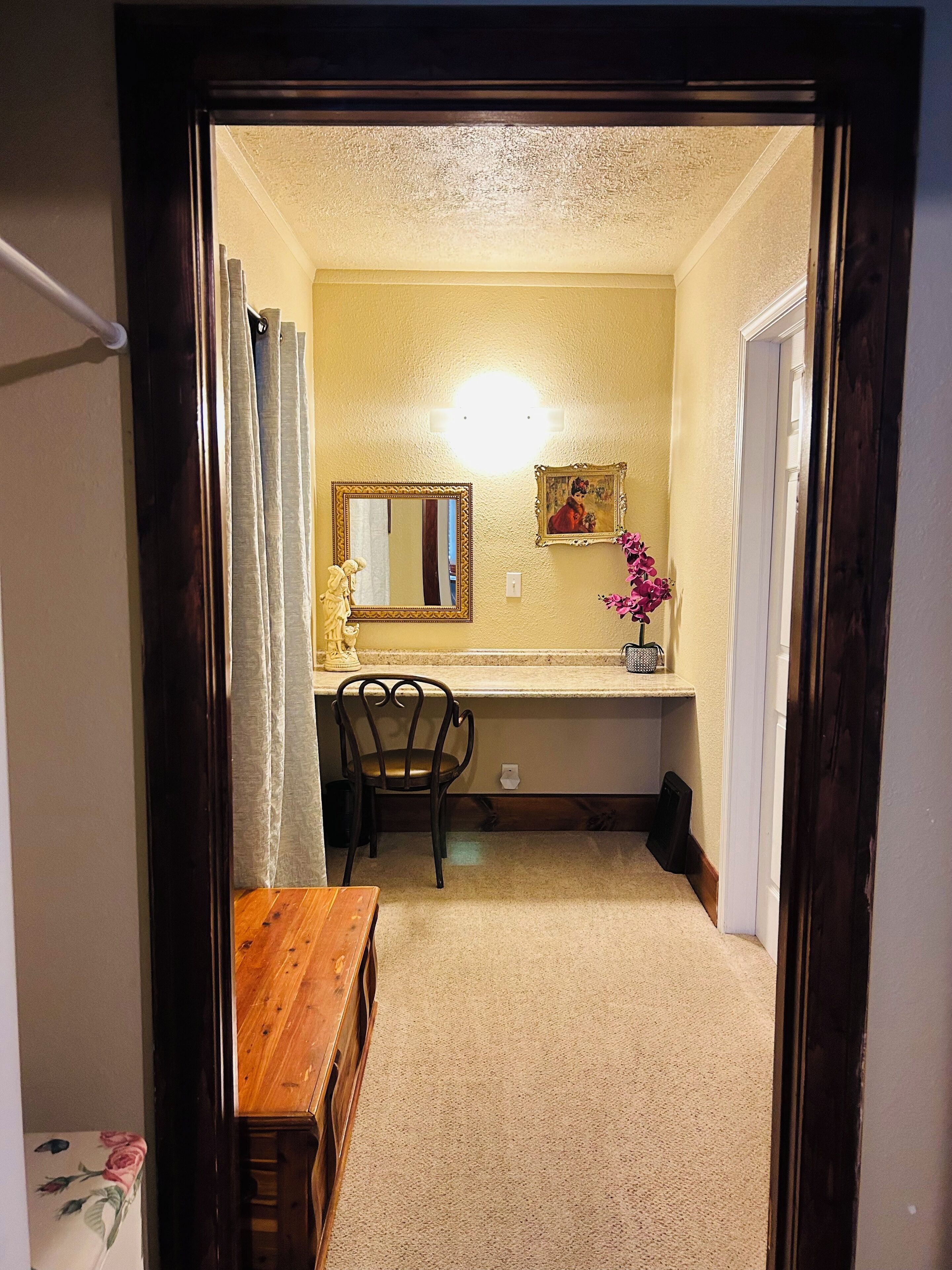 A hallway with a wooden bench, a chair, a small table, a mirror, and a picture frame on the wall.