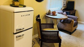 Un espace de vie compact comprenant un réfrigérateur Galanz blanc, une table à manger avec deux chaises, un canapé marron et une horloge murale.