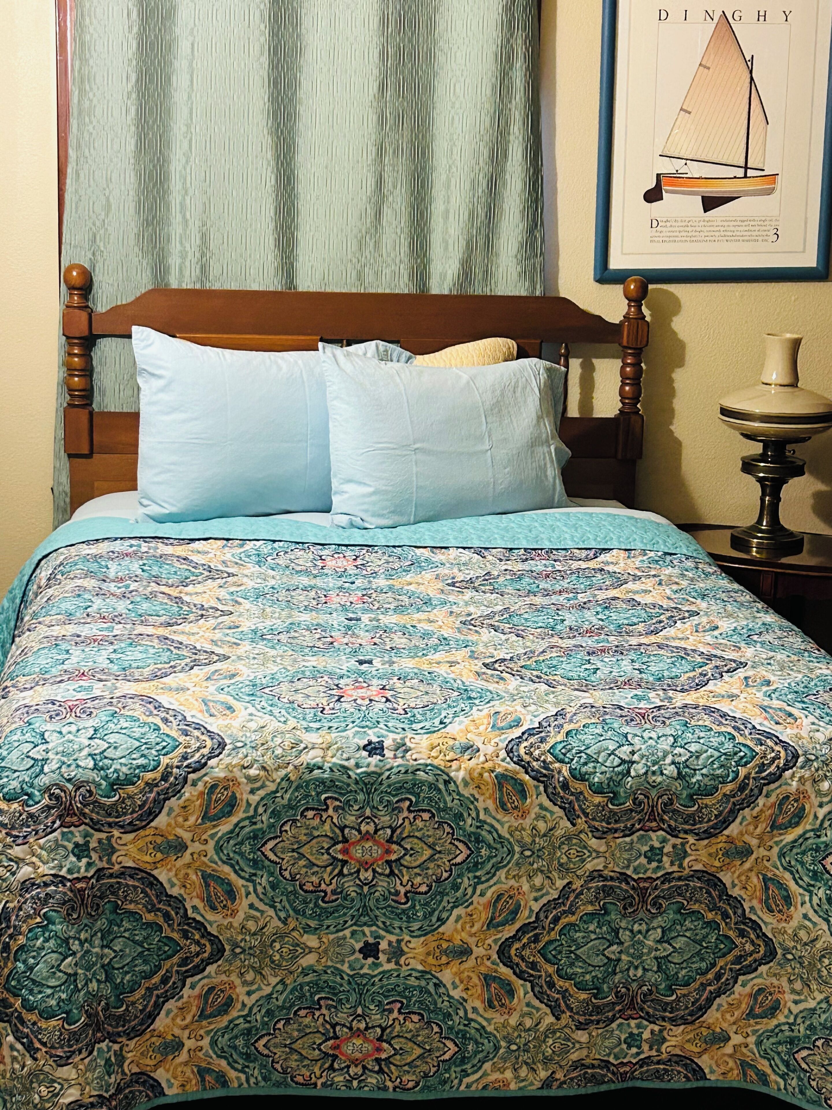 A bed with a patterned bedspread, a wooden headboard, and a framed picture on the wall.