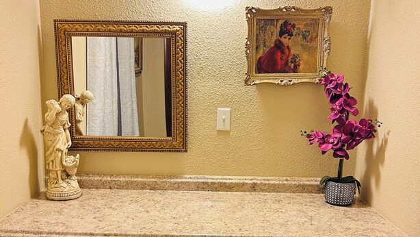Une salle de bain avec un meuble-lavabo, un miroir, un tableau encadré, une statue et une plante en pot.