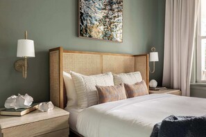 A neatly arranged bedroom with a large bed, two bedside tables, a wall-mounted lamp, a decorative piece, and a window with curtains.