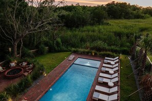 Une piscine rectangulaire bordée de briques, entourée d’une végétation luxuriante et d’arbres.