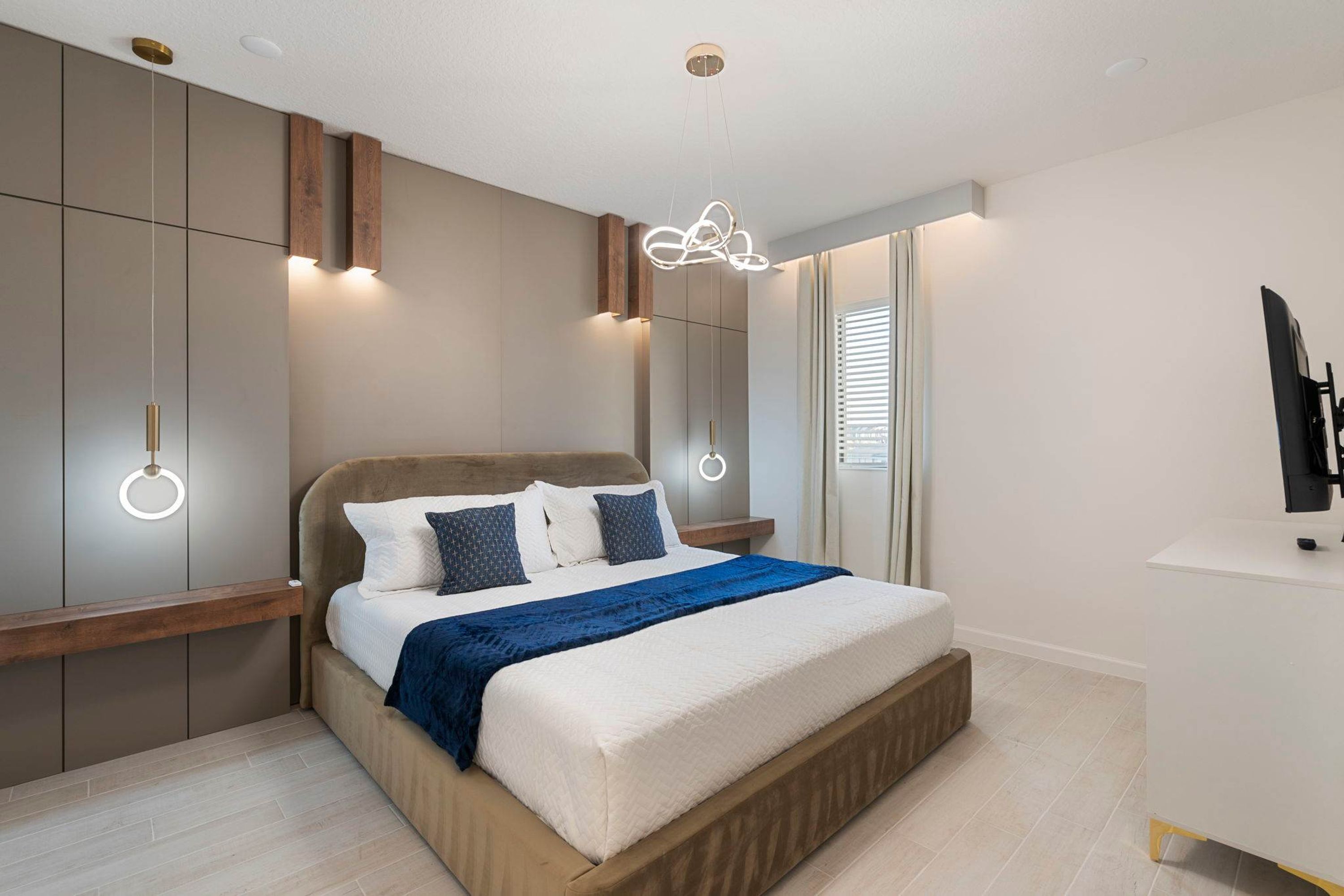 Ein modernes Schlafzimmer mit einem großen Bett, einem festen Holzkopfteil, Nachttischen und einem an der Wand montierten Fernseher.
