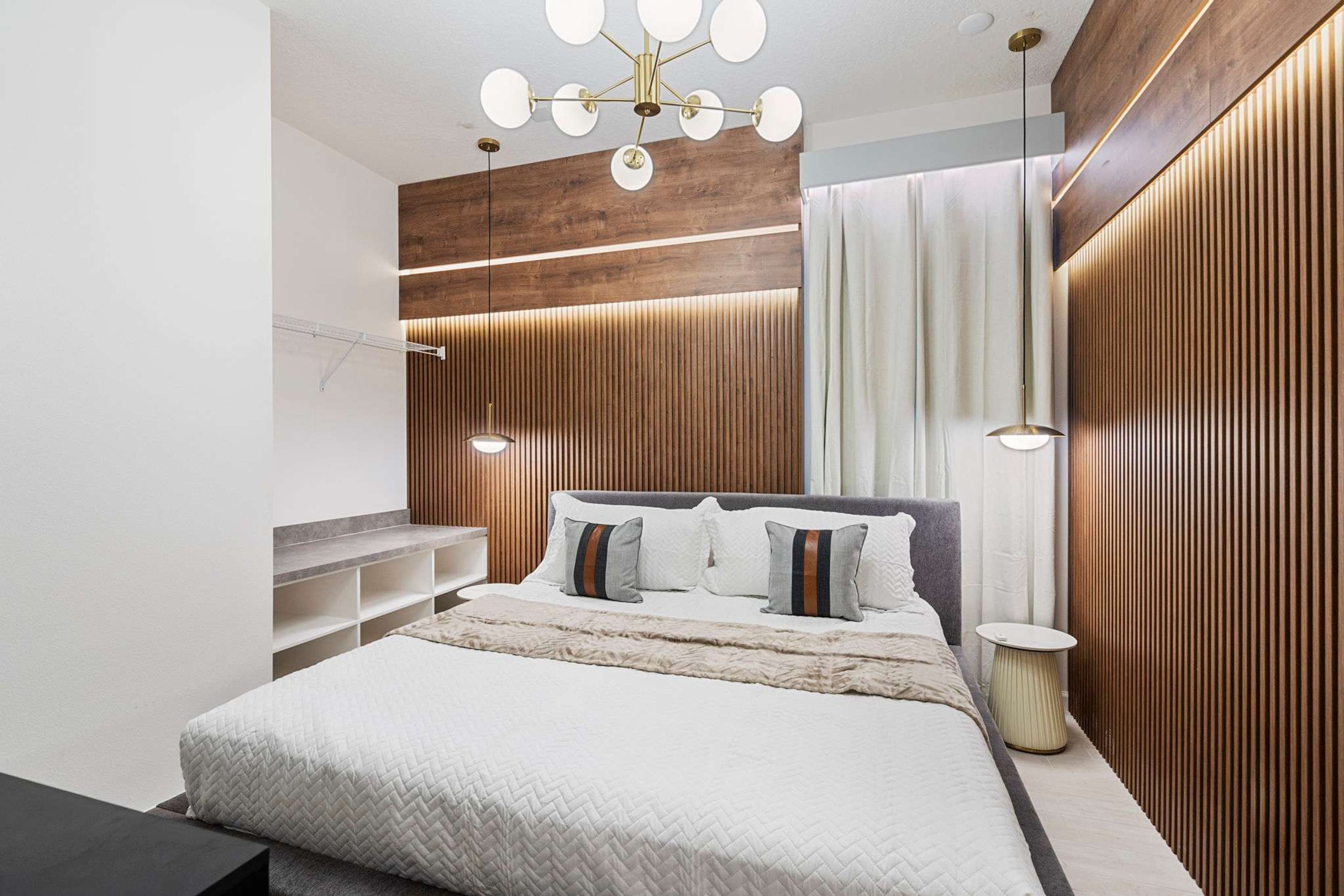 Un dormitorio moderno con una cama grande, estanterías empotradas, un panel de pared de madera e iluminación colgante.