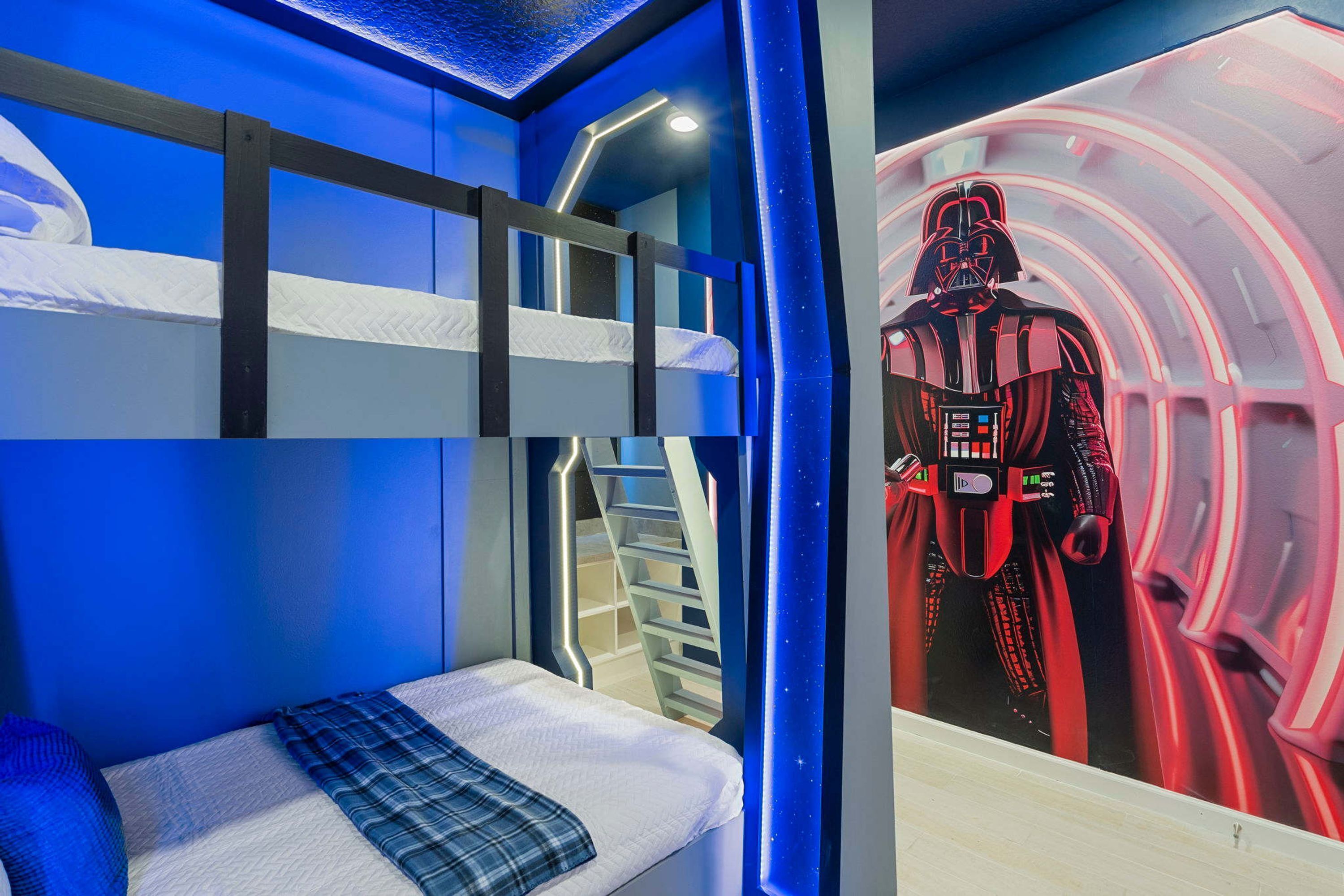 A bunk bed room with a Star Wars themed mural, a staircase, and a blue-lit ceiling.