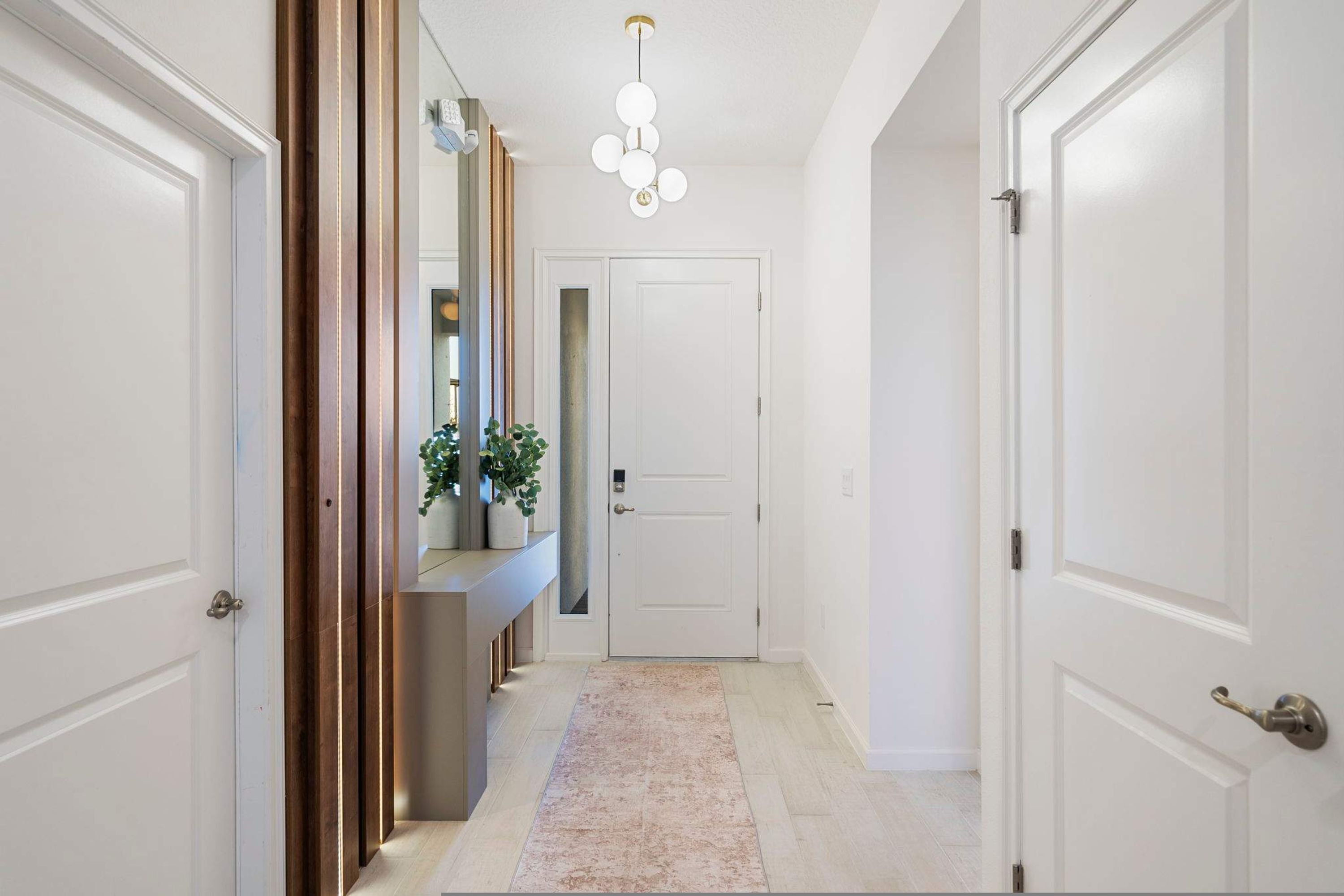 Un couloir avec des portes blanches, un tapis de couleur claire et un luminaire suspendu.