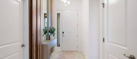 Un couloir avec des portes blanches, un tapis de couleur claire et un luminaire suspendu.