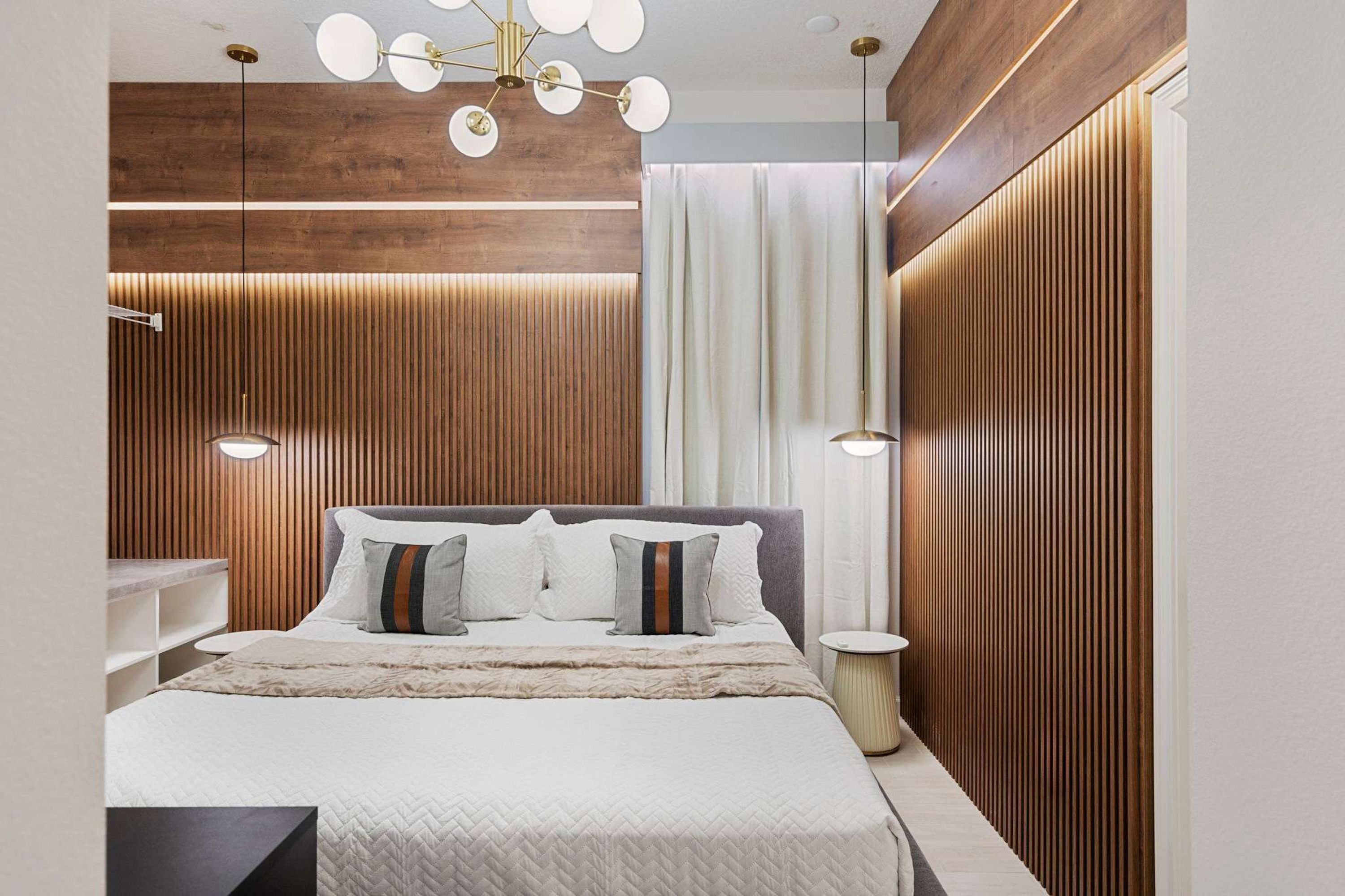 Une chambre moderne avec un mur recouvert de panneaux en bois, un grand lit avec de nombreux oreillers et un luminaire suspendu au plafond.