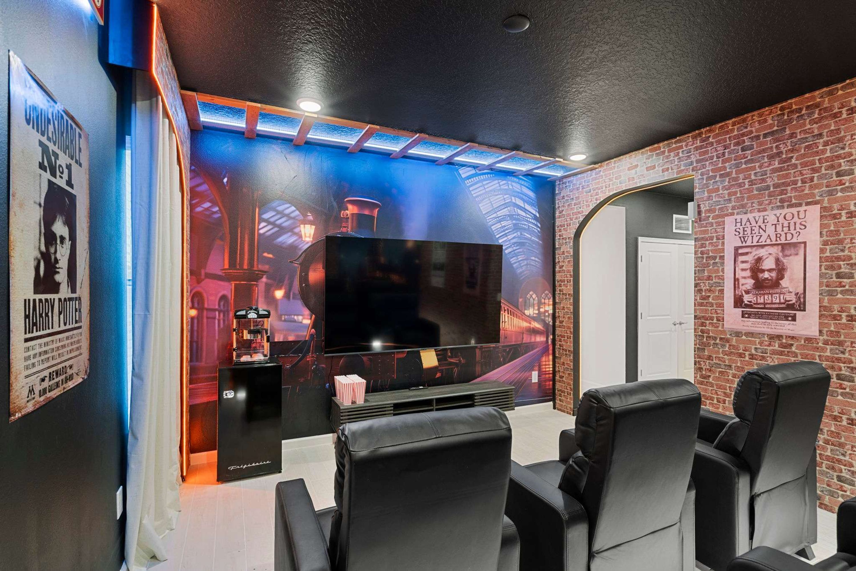 A home theater with a large flat-screen TV, black leather recliner chairs, and a brick wall backdrop.