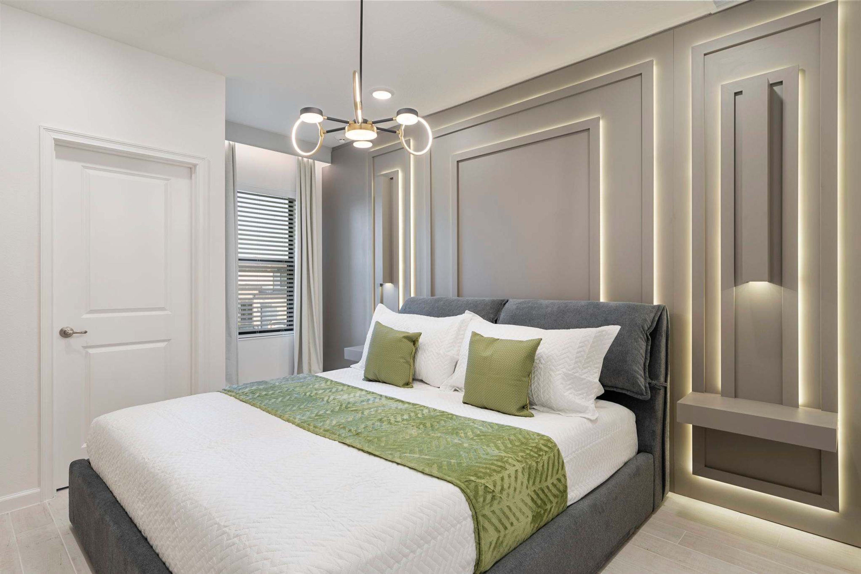 A modern bedroom with a large bed, a green throw blanket, and a unique wall-mounted light fixture.