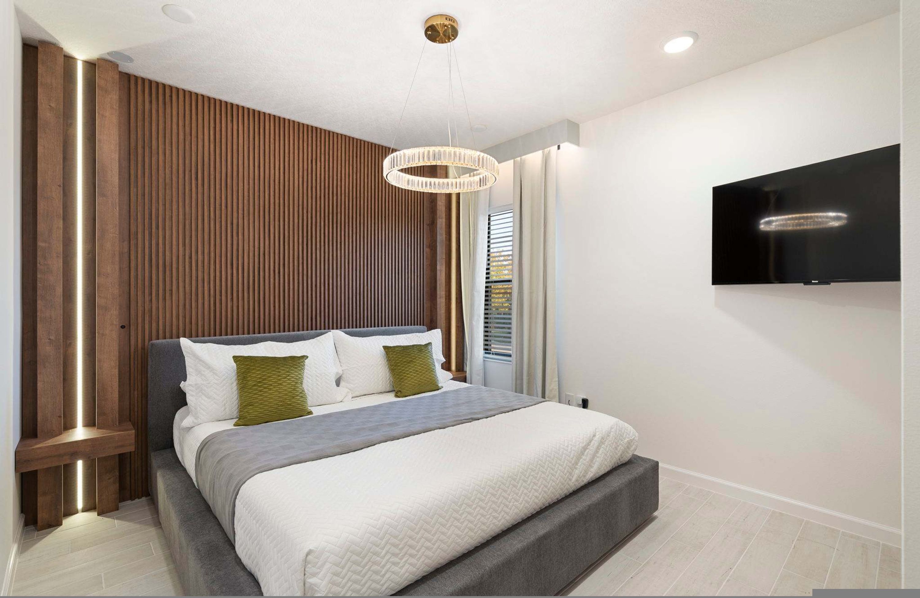 Ein modernes Schlafzimmer mit einem Bett, einem an der Wand montierten Fernseher und einer Wand mit Holzakzenten.