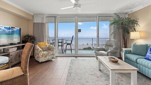Un salón espacioso con televisión, una silla de mimbre, sofá y vistas a la playa a través de grandes puertas correderas.
