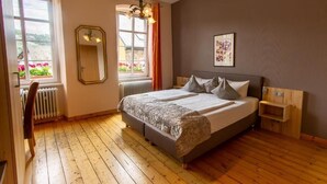 A bedroom with a bed, a window with curtains, a radiator, a wooden chair, and a wall-mounted shelf. - Weinhof Gassen (Kröv)