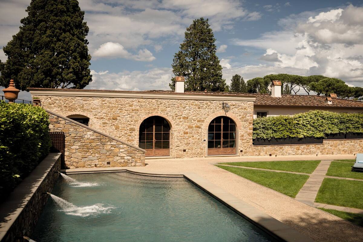 A stone building with a pool, arched windows, and a well-maintained lawn with lounge chairs.