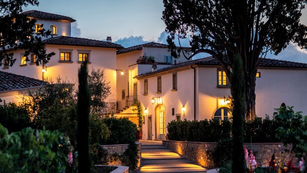 A multi-story building with a central staircase leading to a door, surrounded by greenery and stone walls. - Dimora Ghirlandaio (Impruneta)