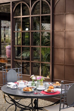 Een ronde tafel gedekt voor het ontbijt, met borden eten, kopjes en een vaas bloemen.