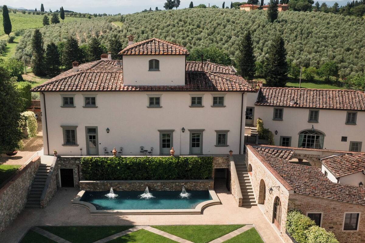 A large villa with a swimming pool, terraced roof, and lush gardens.