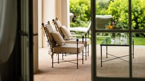 A sunlit patio with a glass table and chairs, a hanging lantern, and a view of lush greenery. - Dimora Ghirlandaio (Impruneta)