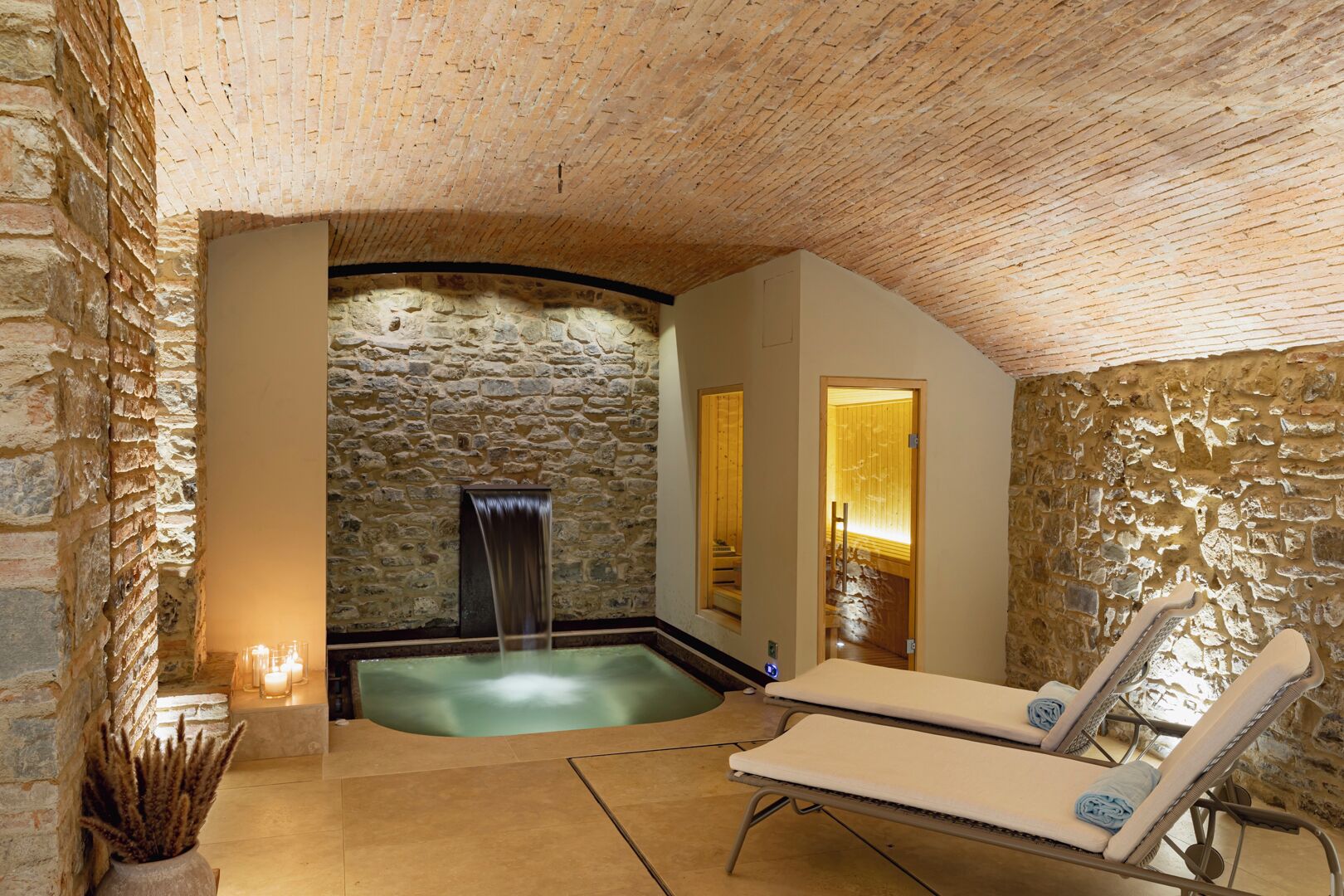Ein Wellnessbereich mit Steinwand, Whirlpool und zwei Liegestühlen.