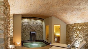 A spa area with a stone wall, a hot tub, and two lounge chairs. - Dimora Ghirlandaio (Impruneta)