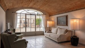 A cozy room with a stone ceiling, a large arched window, a beige sofa, two armchairs, and a painting on the wall. - Dimora Ghirlandaio (Impruneta)