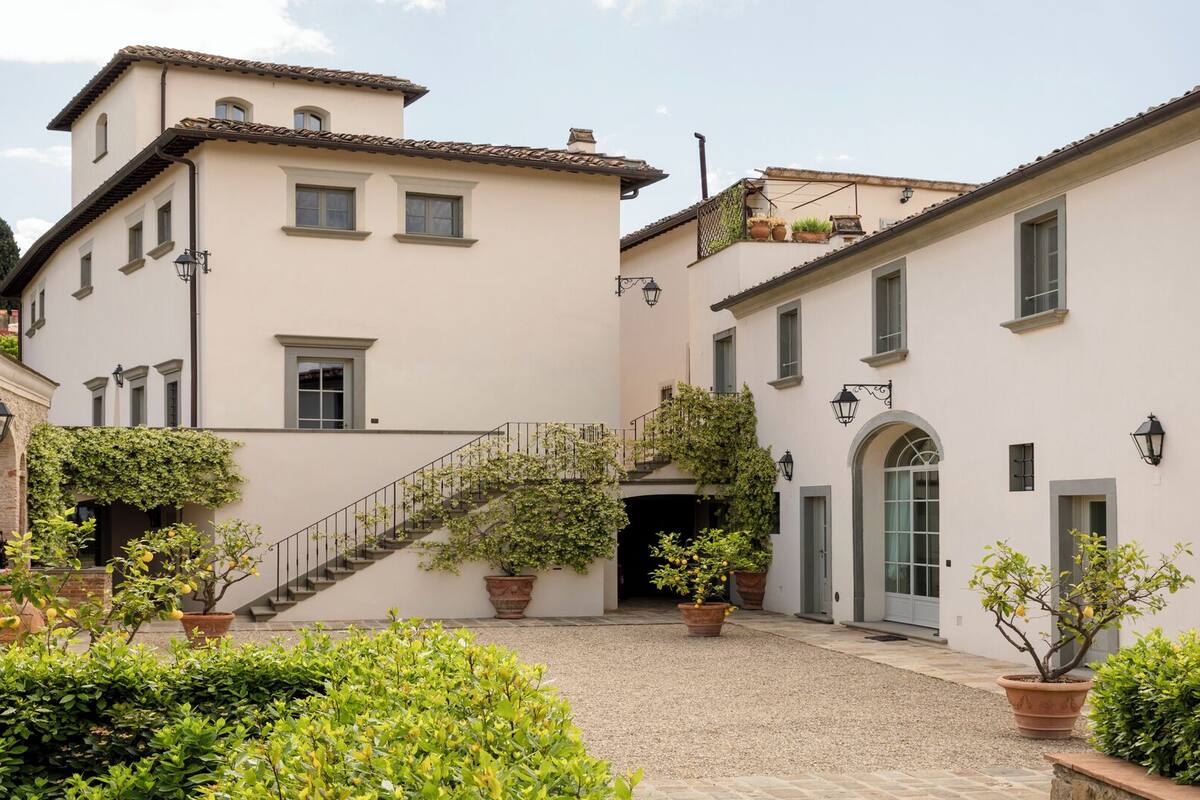 A courtyard with a staircase leading to a second floor, surrounded by buildings with white walls and terracotta roofs.