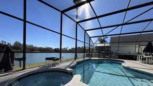 A swimming pool with a hot tub, surrounded by a covered area with a view of a lake. - Lakeside at Lake Berkley close to Disney (Kissimmee)